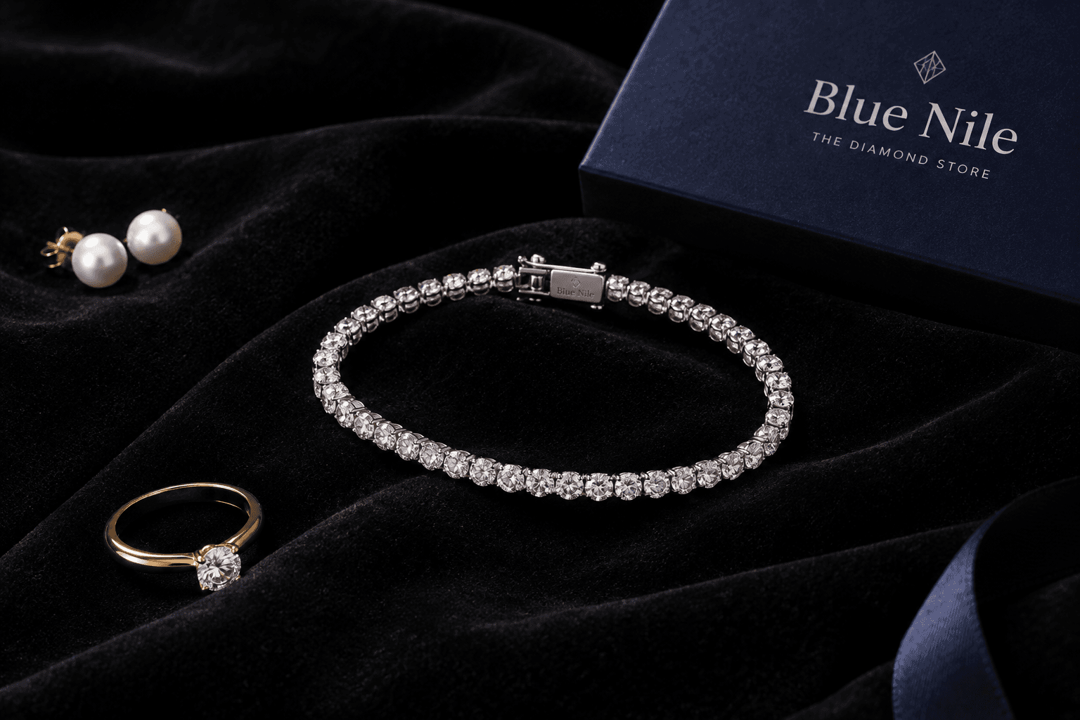 یک دستبند تنیس الماس از برند Blue Nile با الماسهای درخشان روی زمینهی مخمل مشکی، همراه با چند قطعه جواهر دیگر مانند حلقه و گوشواره.